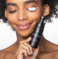 Modelo negra sonriente con cabello rizado usando el champú Lash & Brow