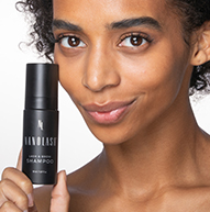 Modelo negro sonriente con cabello rizado sosteniendo el champú Lash & Brow